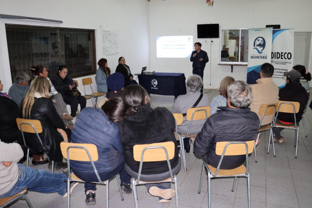 Grupo de personas asistiendo a una charla en un salón comunal.