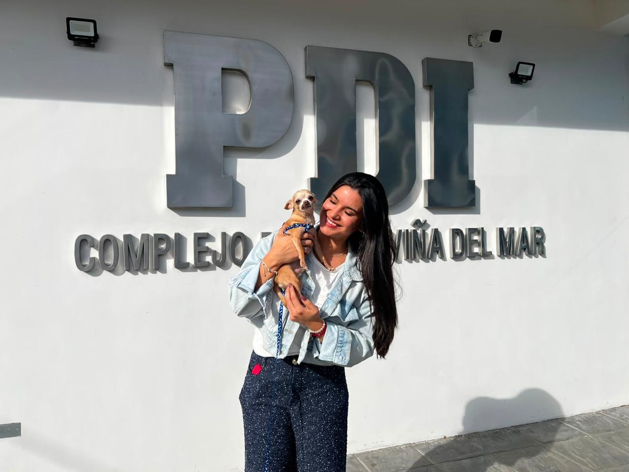 Mujer sonriente sosteniendo un perro Chihuahua frente a las siglas