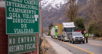 Señalética verde de "Unidad Internacional Campamento Guardia Vieja Dirección de Vialidad" y "No entrar recinto fiscal", con camiones y un vehículo en fila en una carretera al fondo.