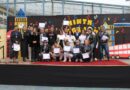 Estudiantes y docentes posan con certificados y medallas en un escenario decorado con motivos de Londres durante el English Song Festival.
