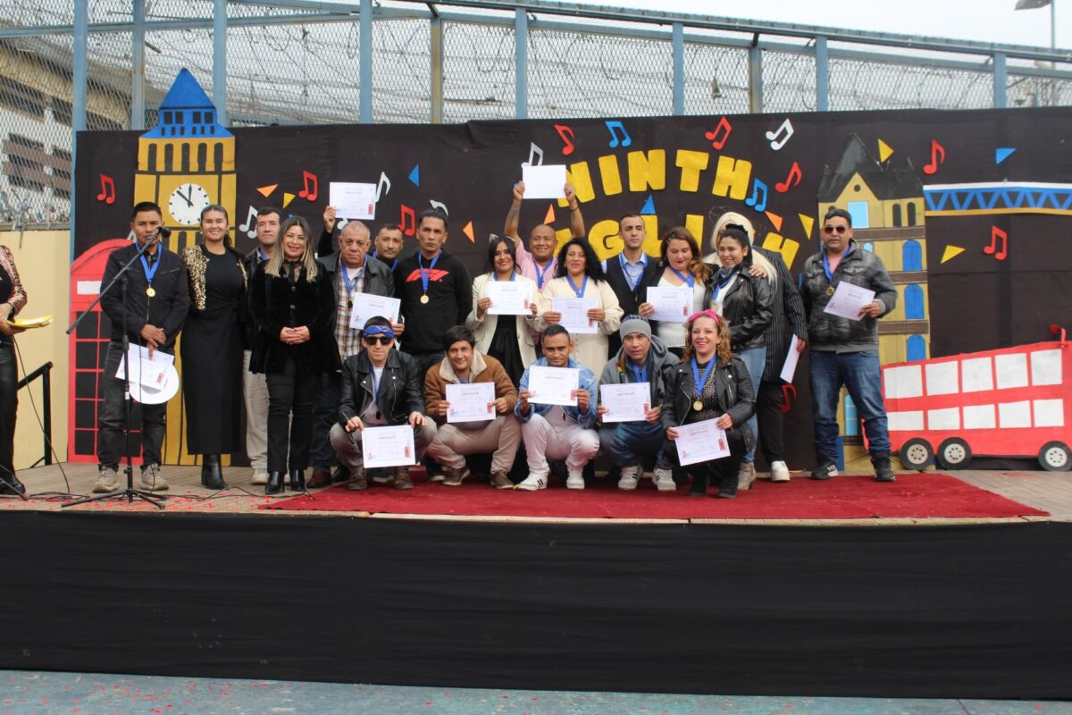 Estudiantes y docentes posan con certificados y medallas en un escenario decorado con motivos de Londres durante el English Song Festival.