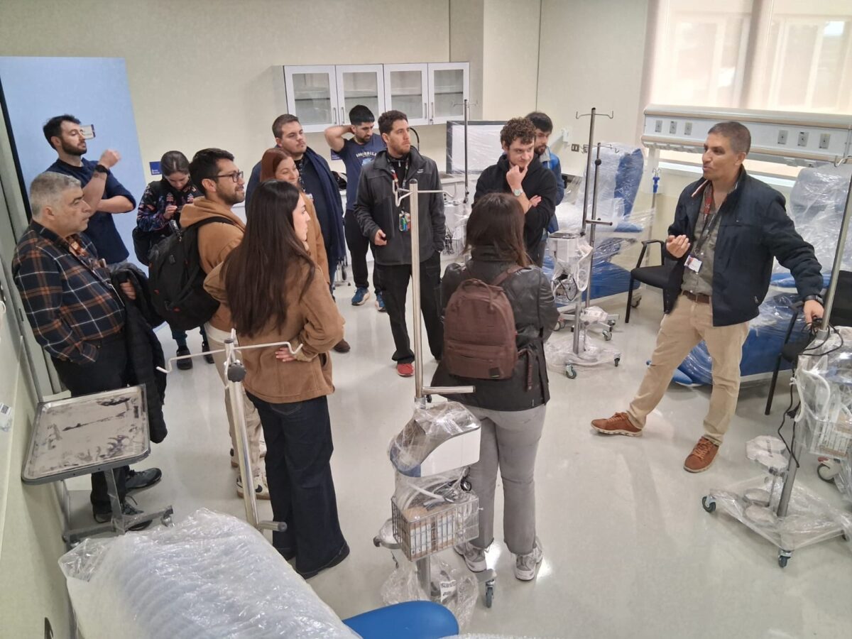 Grupo de médicos observando y escuchando a un profesional dentro de una sala equipada con mobiliario médico.