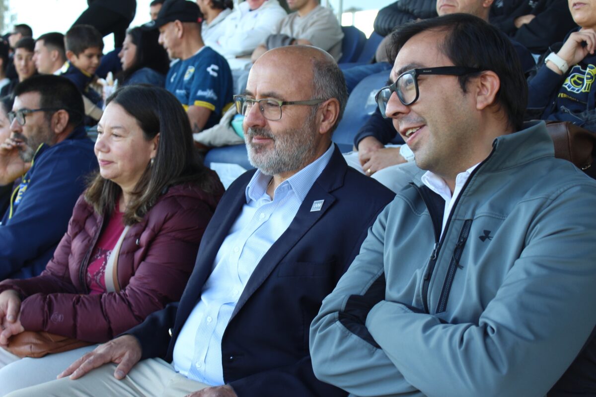 Primer plano de tres personas sentadas en graderías de un estadio.