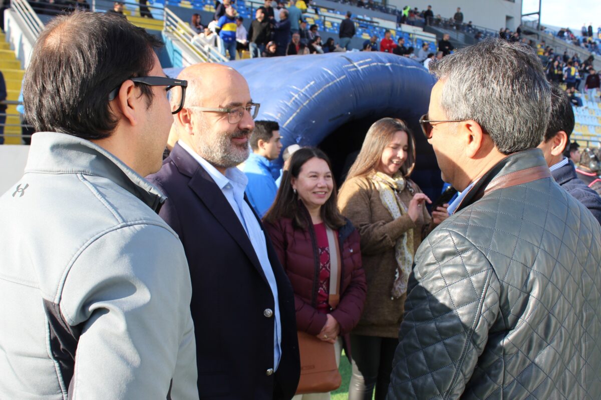 Un grupo de personas conversando en el borde de una cancha de fútbol.