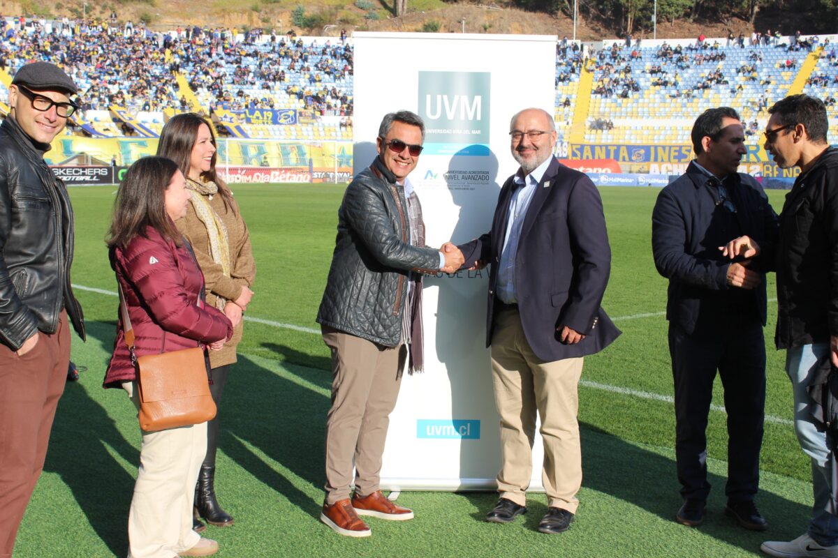 Grupo de personas posando frente a un banner de la UVM en un campo de fútbol.