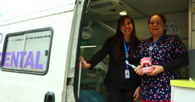 Dos mujeres sonriendo frente a una unidad dental móvil, una sostiene un modelo de dientes.