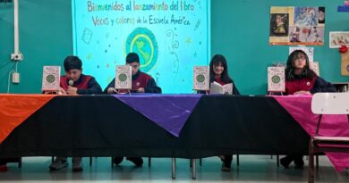 Estudiantes de séptimo básico sentados detrás de una mesa cubierta con manteles de colores, presentando libros.