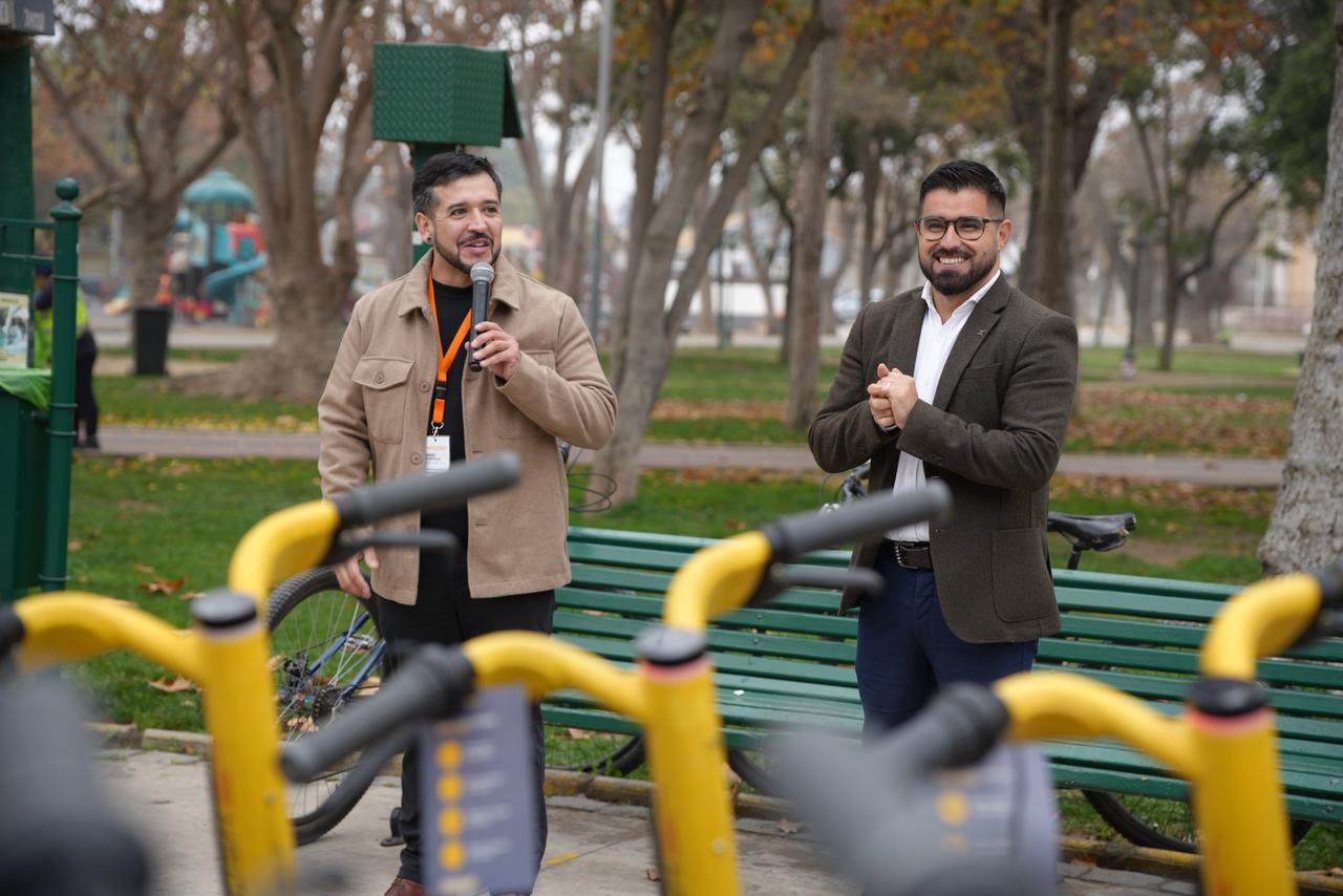 Dos hombres hablando en un evento al aire libre, con bicicletas amarillas en primer plano.