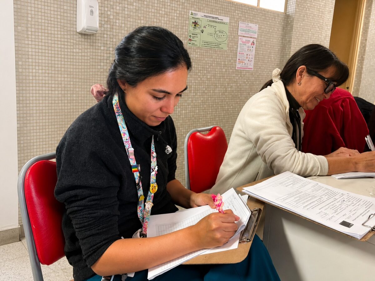 Dos mujeres sentadas en sillas rojas, concentradas revisando documentos en una mesa.