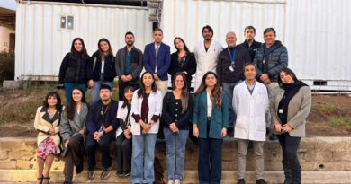 Grupo numeroso de profesionales de la salud posando para una fotografía grupal frente a contenedores blancos.