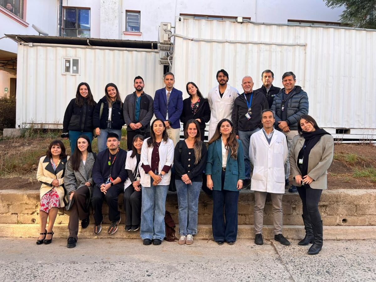 Grupo numeroso de profesionales de la salud posando para una fotografía grupal frente a contenedores blancos.