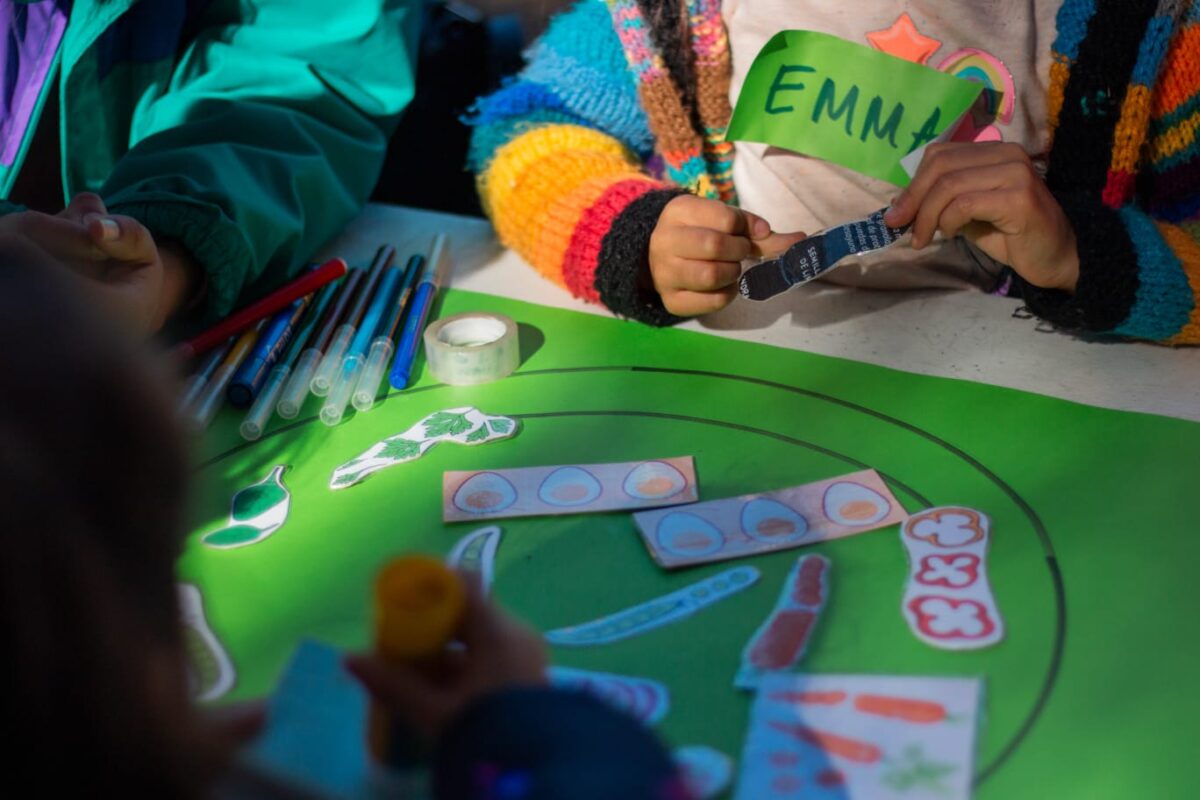 Niños participando en una actividad creativa con materiales sobre una mesa verde.