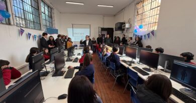 Estudiantes y adultos en un laboratorio de computación con pantallas encendidas y proyectando una imagen en la pared.
