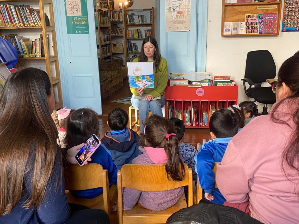 Una mediadora de lectura muestra un libro ilustrado a un grupo de niños sentados en la biblioteca.