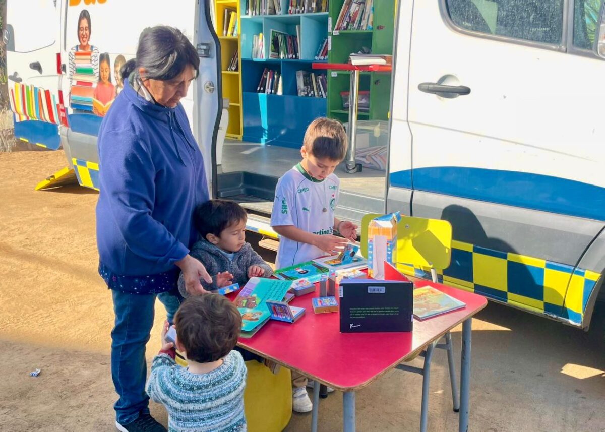 Niños y adultos interactuando con libros junto al Bibliobús Municipal de Zapallar.