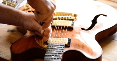 Manos de un luthier trabajando minuciosamente en la mantención y reparación de una guitarra eléctrica de cuerpo de madera.