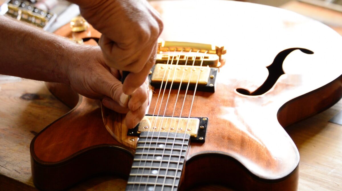 Manos de un luthier trabajando minuciosamente en la mantención y reparación de una guitarra eléctrica de cuerpo de madera.