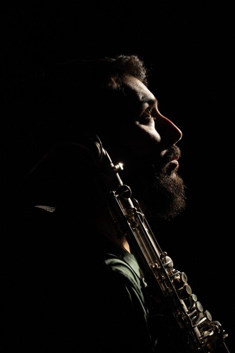 Retrato de perfil en penumbra del músico Gerardo Saks con su saxofón.