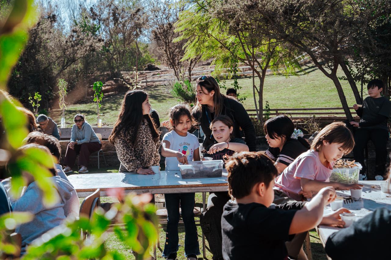Niños y niñas participando en un taller de plantación y cuidado de tierra en mesas de trabajo.