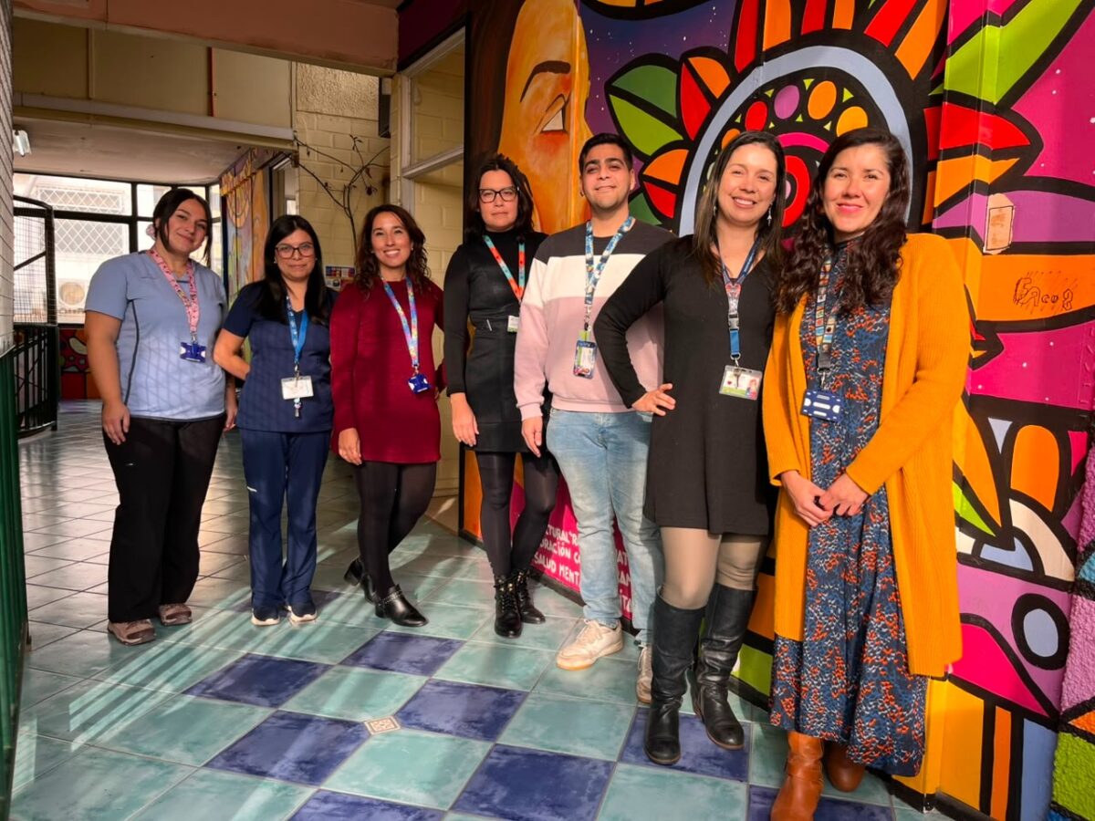 Miembros del equipo de salud mental comunitaria posando junto a un mural colorido.