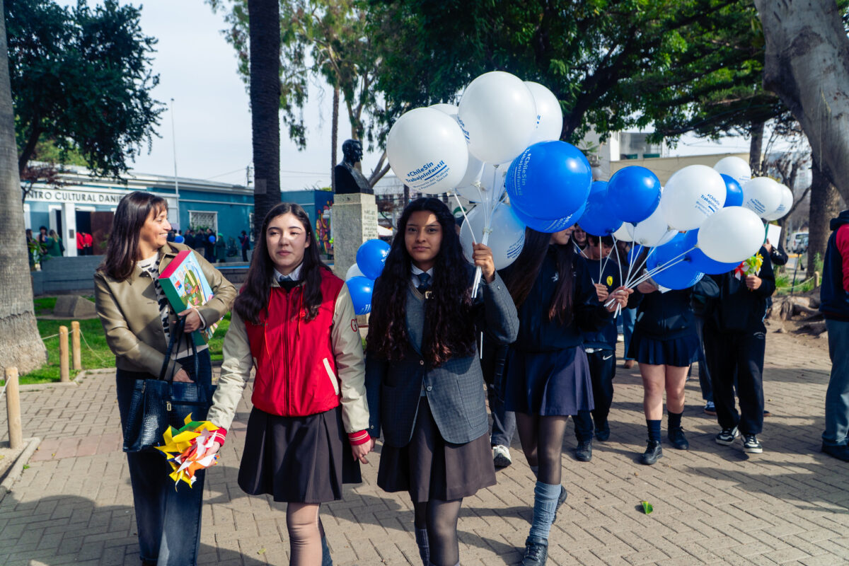 Jóvenes con globos azules y blancos caminan al aire libre.