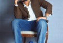 El músico chileno Bastián Juan posando sentado con lentes de sol y chaqueta café.