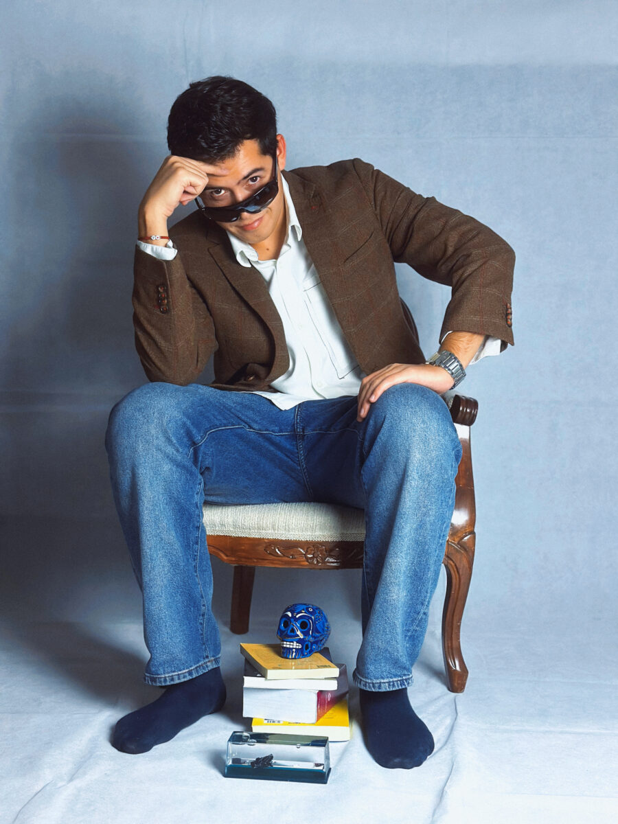 El músico chileno Bastián Juan posando sentado con lentes de sol y chaqueta café.