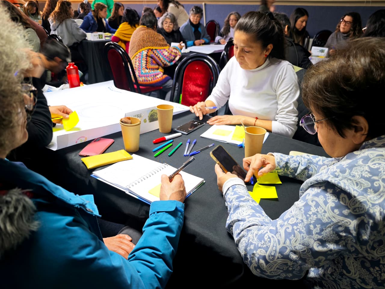Mujeres trabajando en mesas de trabajo colaborativo durante el taller de agronegocios.