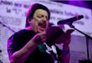 Mauricio Redolés cantando en vivo con micrófono y libro en mano.