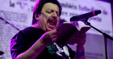 Mauricio Redolés cantando en vivo con micrófono y libro en mano.