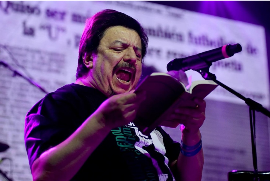 Mauricio Redolés cantando en vivo con micrófono y libro en mano.