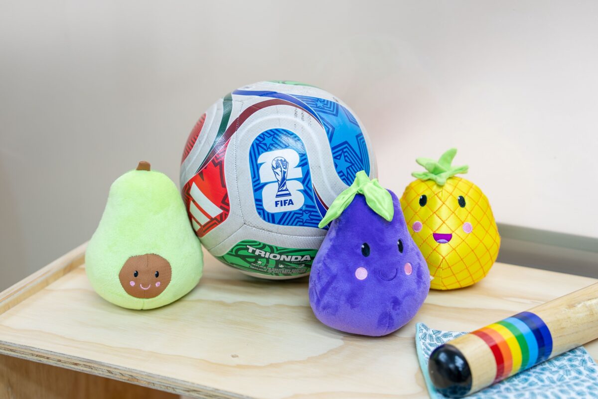 Balón de fútbol junto a peluches con forma de frutas, elementos para el aprendizaje infantil.