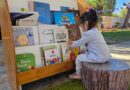 Niña pequeña seleccionando un libro en una biblioteca infantil al aire libre.