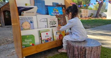 Niña pequeña seleccionando un libro en una biblioteca infantil al aire libre.