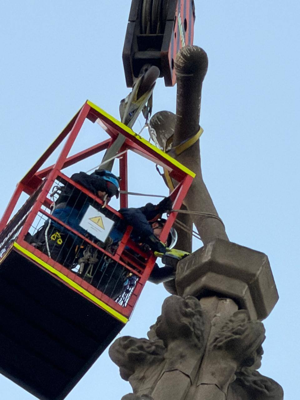 Funcionarios municipales en una jaula de altura asegurando la cruz en la punta de la torre de la iglesia.