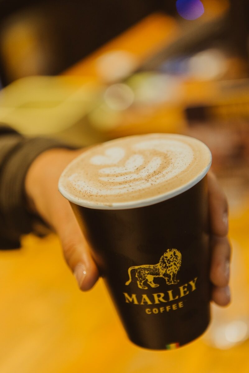 Mano sosteniendo un vaso de café con arte latte.