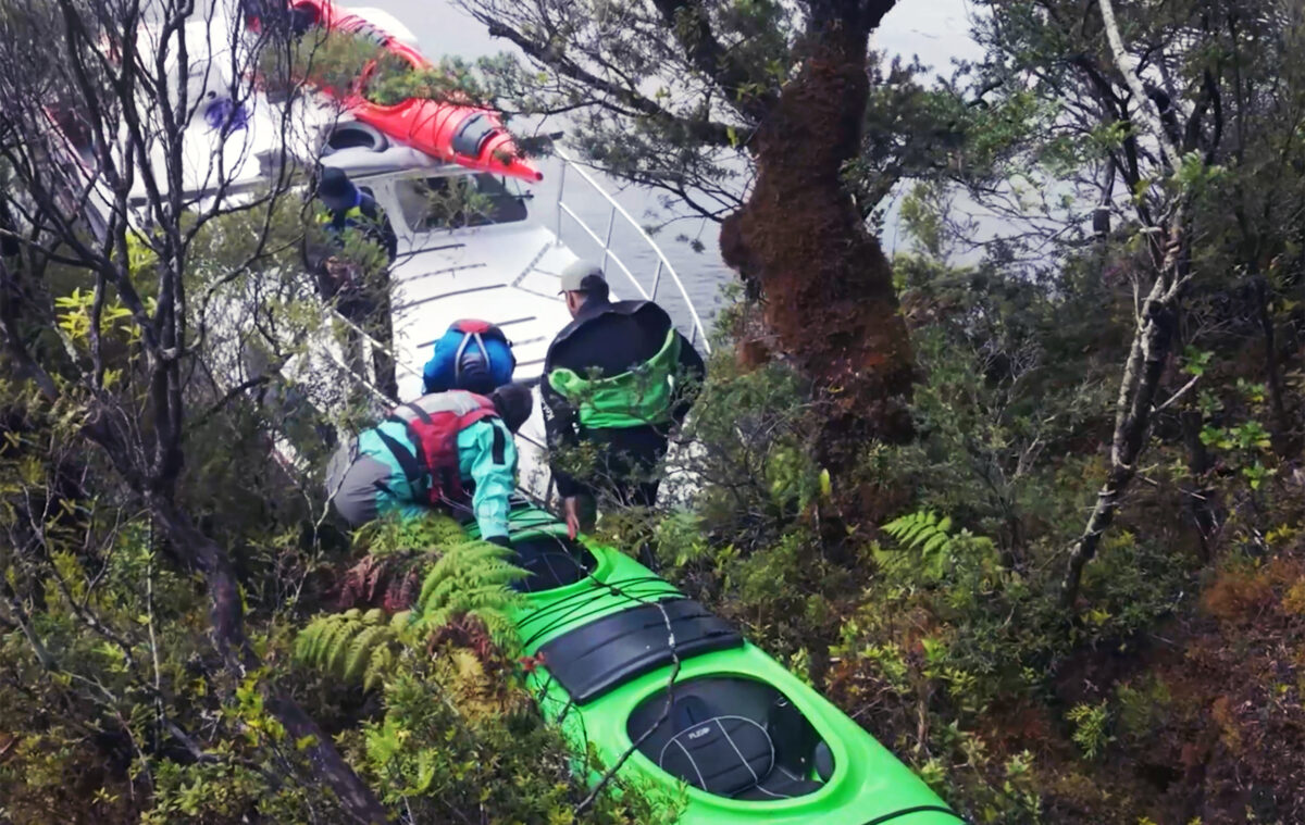 Equipo de El clan transportando kayaks a través de un bosque en la Patagonia.
